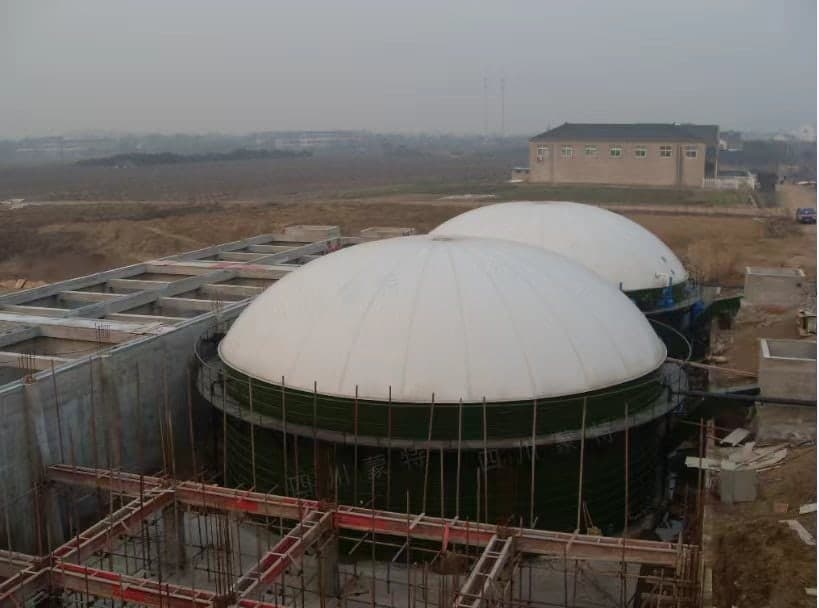 A site during civil works, with white membrane roofs on two tanks.