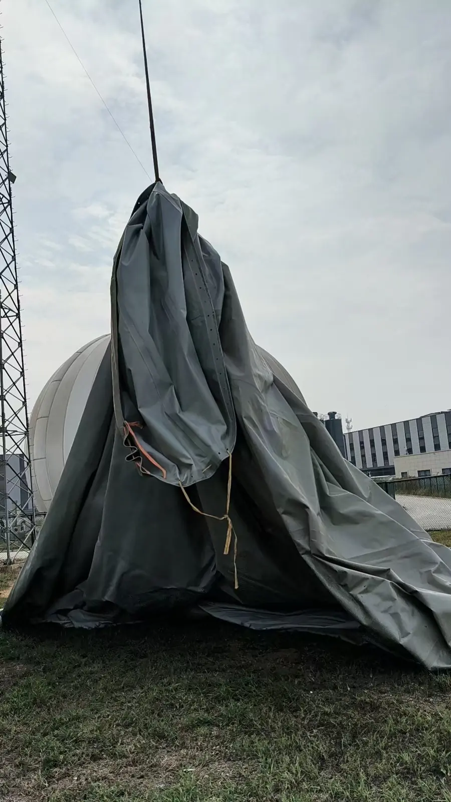 起重机在地面区域提起收拢的膜体，周围设有牵引绳带。